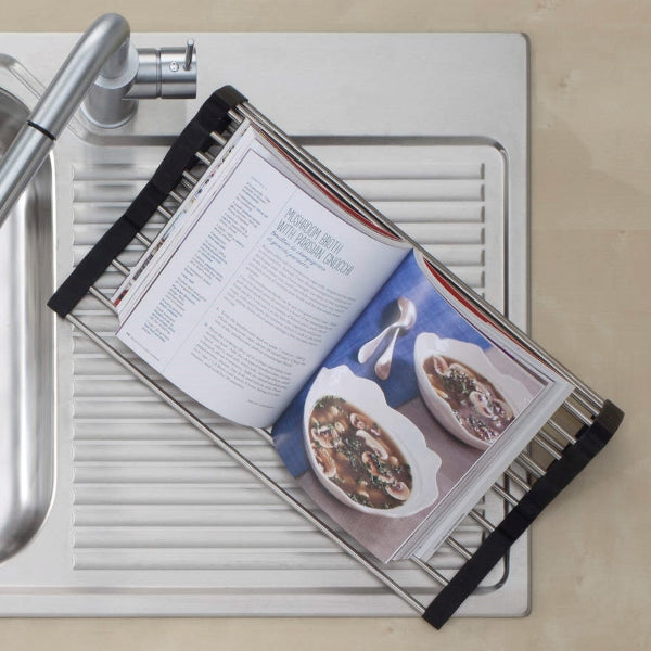 Oliveri Cooking Mate Foldamate stainless steel dish rack over kitchen sink, shown with cookbook open in use