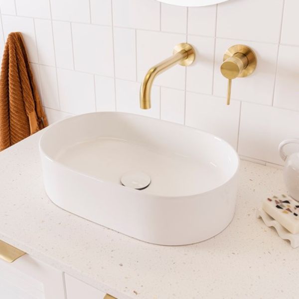 ADP Patty gloss white oval above counter basin on a speckled benchtop with brass wall tapware in an ensuite-style bathroom