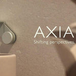 Phoenix Axia matte black wall top assembly on textured wall, shown in lifestyle setting with AXIA branding and tap handle detail