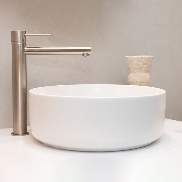 Phoenix Vivid Slimline vessel mixer in brushed nickel beside an above-counter basin, side view on benchtop