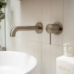 Nero Mecca wall-mounted basin/bath spout in brushed nickel, shown over a bathroom basin and vanity bottle