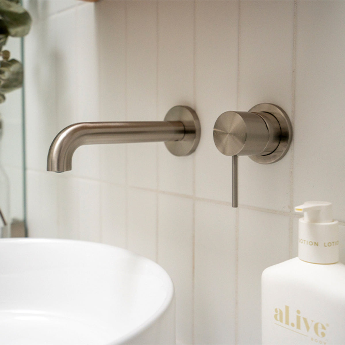 Nero Mecca wall-mounted basin/bath spout in brushed nickel, shown over a bathroom basin and vanity bottle