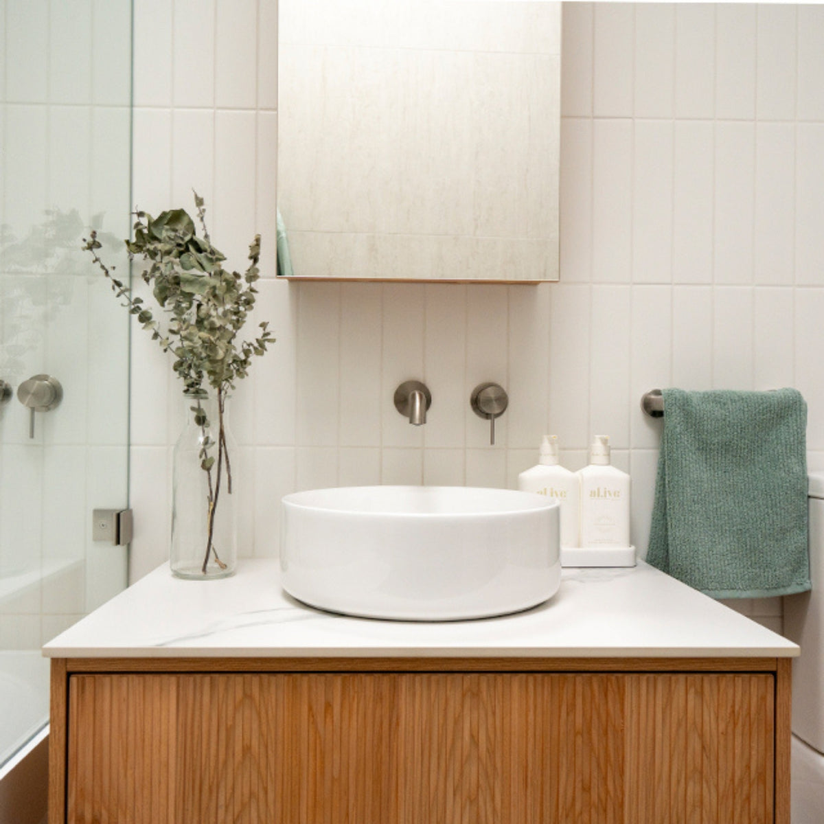 Nero Mecca brushed nickel wall-mounted basin/bath spout above a white vanity and round basin in a bathroom setting