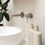 Nero Mecca wall-mounted basin/bath spout in brushed nickel, shown over a white basin with matching wall outlet in a bathroom.