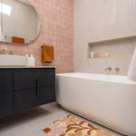 Nero Mecca brushed gold wall-mounted basin/bath spout in a bathroom, with bathtub and vanity styling visible