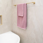 Nero Mecca Care brushed gold grab rail used as a towel rail in a tiled bathroom, with pink towels hanging on it