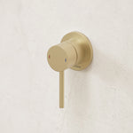 Caroma Liano II wall-mounted bath/shower mixer in brushed brass, with round plate and single lever on white wall