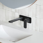 Caroma Luna black wall-mounted basin/bath mixer set above a white basin and tiled wall
