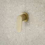 Caroma Contura II wall-mounted bath/shower mixer in brushed brass with single lever on speckled stone tile wall