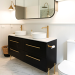 Caroma Liano II brushed brass toilet roll holder on a black vanity in a modern bathroom setting