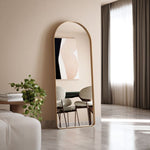 Brushed gold arch full length mirror by Ingrain, floor standing in a modern room with dining chairs and a window.