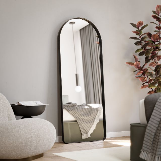 Matte black arch full length mirror by Ingrain leaning in a bedroom, showing a modern floor-standing portrait view.
