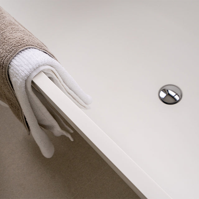 Chrome bath pop-up waste in a white bath, with a towel draped over the edge