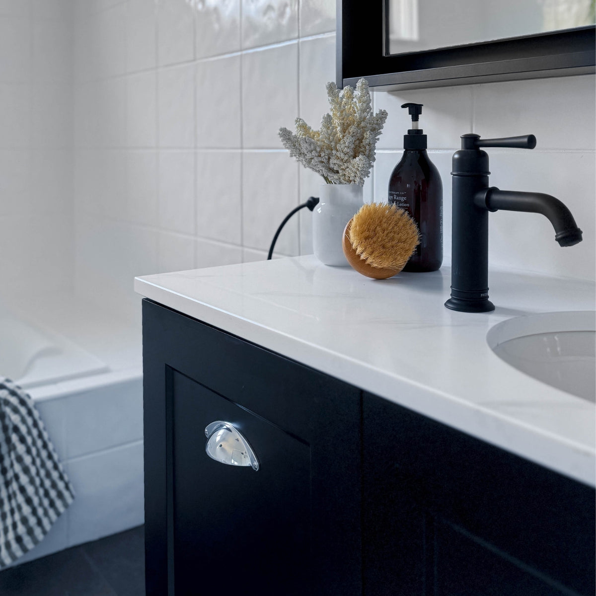 Phoenix Cromford matte black basin mixer on a white vanity, side view in a modern bathroom.