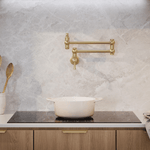 Phoenix Cromford wall mounted pot filler in brushed gold above a cooktop, shown folded flat against a kitchen wall.