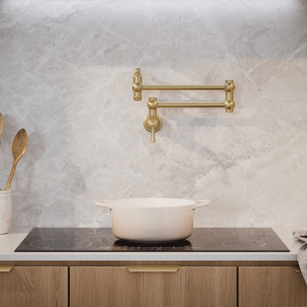 Phoenix Cromford wall mounted pot filler in brushed gold above a cooktop, shown folded flat against a kitchen wall.