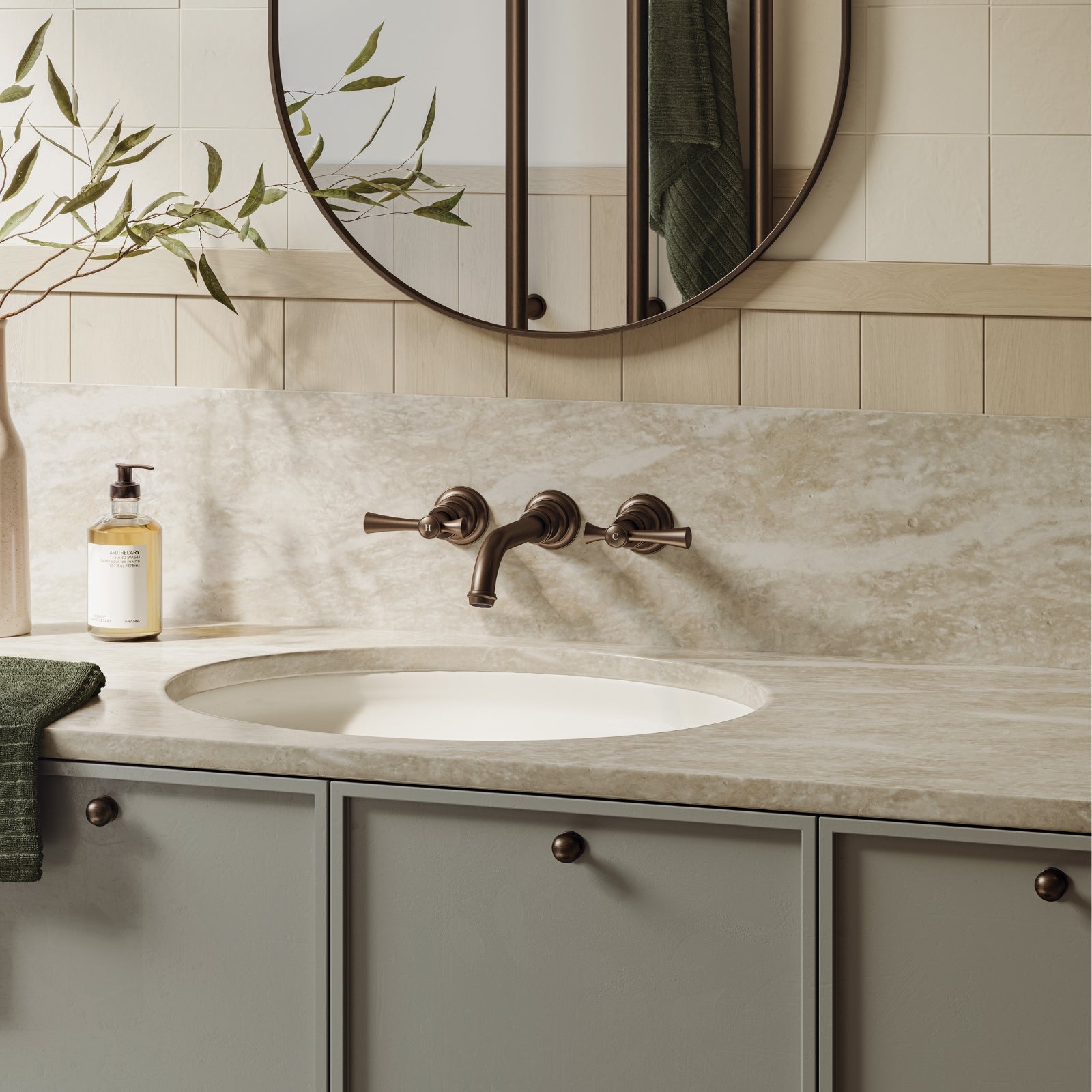 Phoenix Cromford wall basin/bath tap set in brushed bronze, shown above an oval basin in a bathroom vanity setting