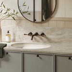 Phoenix Cromford wall basin/bath tap set in brushed bronze, shown above an oval basin in a bathroom vanity setting