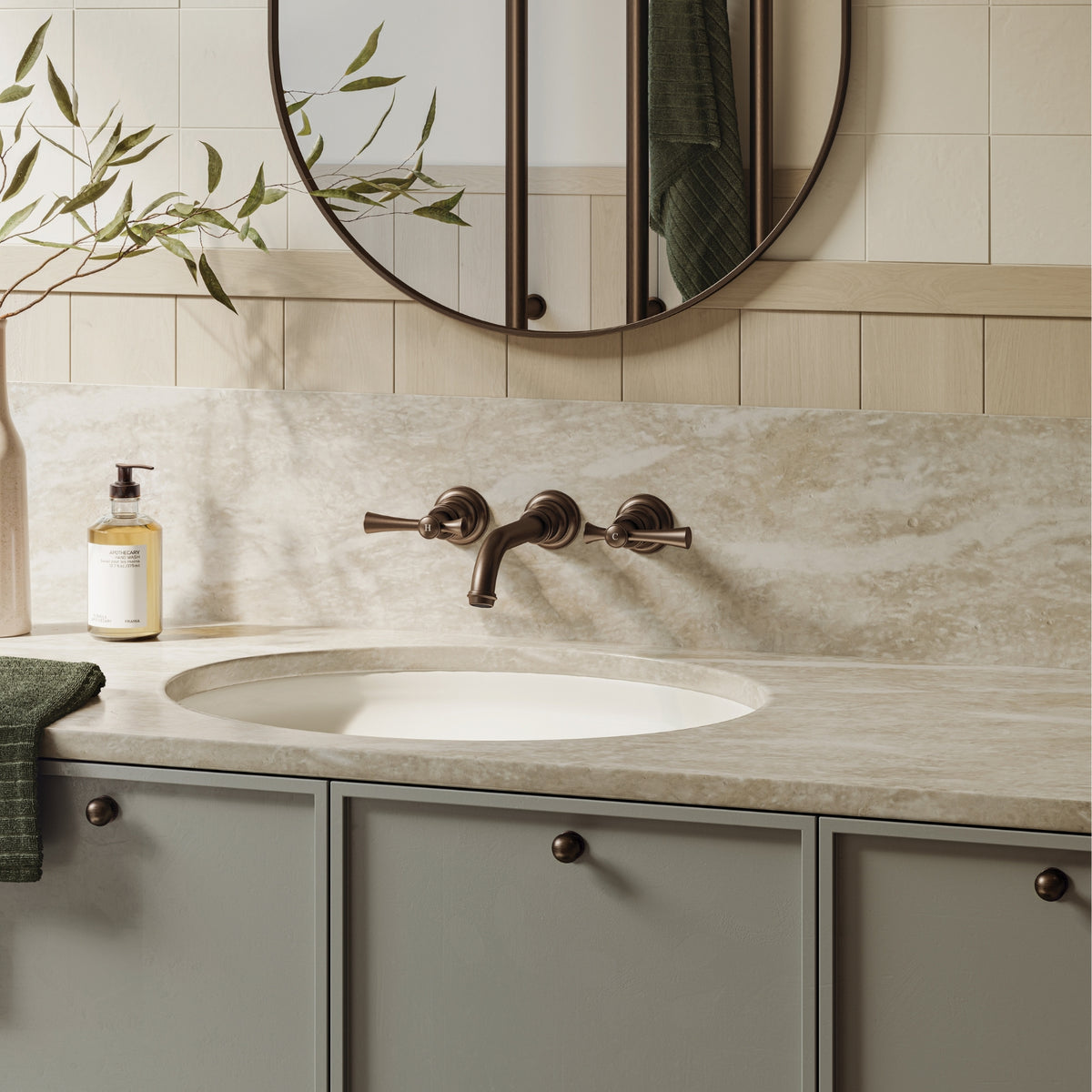 Phoenix Cromford wall basin/bath tap set in brushed bronze, shown above an oval basin in a bathroom vanity setting