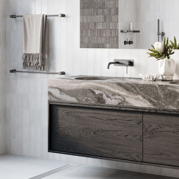 Phoenix Vivid Slimline wall basin mixer set in brushed carbon, curved wall-mounted tap over a marble-look basin in a modern bathroom