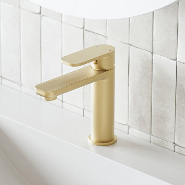 Caroma Luna brushed brass basin mixer on a bathroom vanity, side view against white tiles