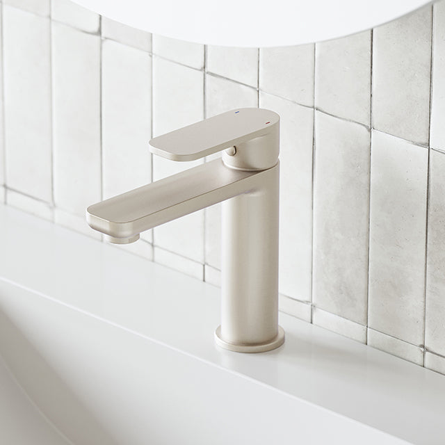 Caroma Luna basin mixer in brushed nickel, side view on white bathroom basin with tiled wall background