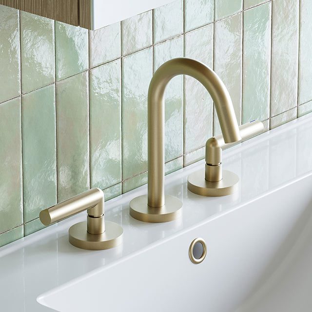 Phoenix Vivid Slimline Plus 3 piece basin tap set in brushed gold, with curved spout and lever handles, on a white basin after.