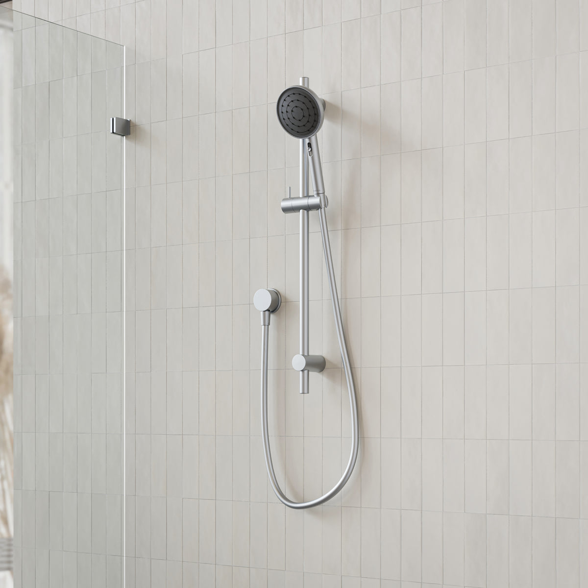 Caroma Urbane II rail shower in brushed nickel, with round handset, hose and wall rail in a tiled bathroom setting
