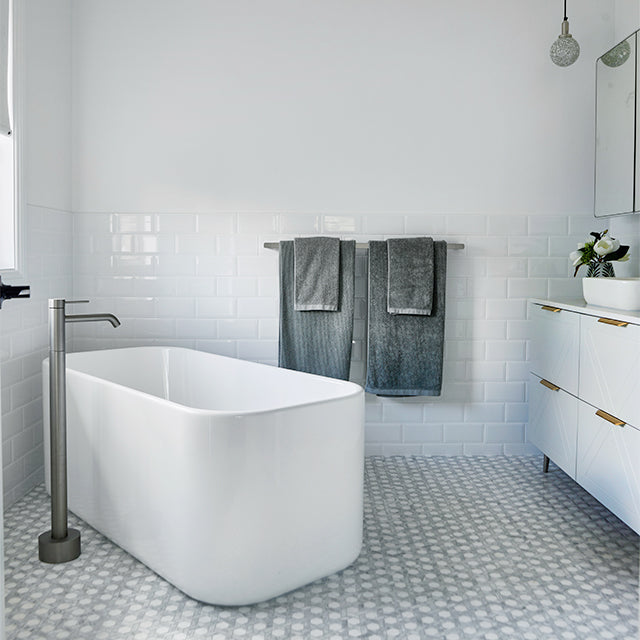 Caroma Liano II freestanding bath filler in brushed nickel beside a white bath in a modern bathroom￼
