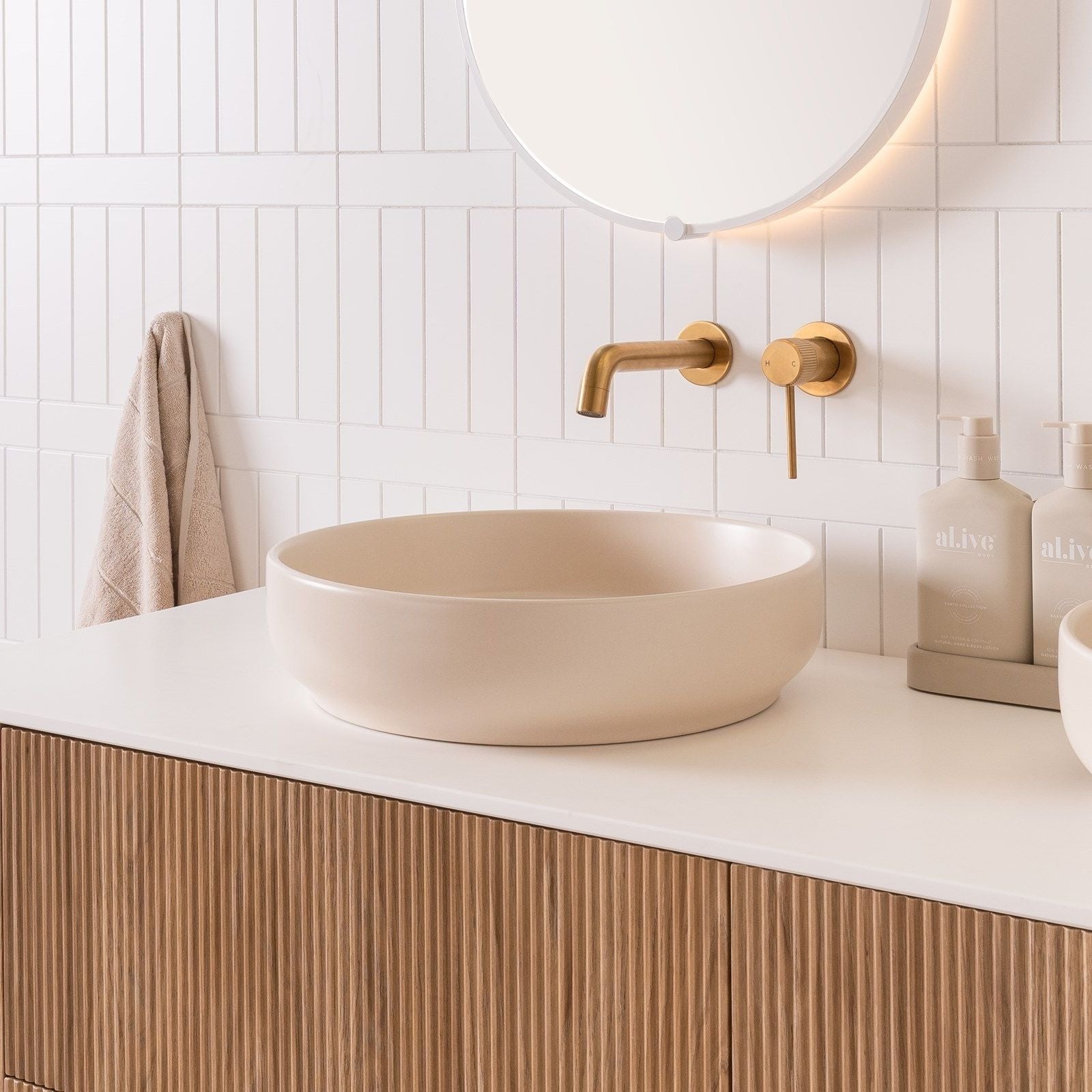 ADP Monroe round above counter basin in matte ivory, shown on a vanity with brushed brass tapware in a bathroom setting