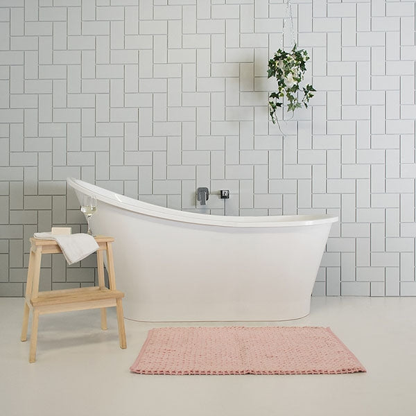 ADP Placido white freestanding bath, oval shape, styled in a modern bathroom with timber stool and pink bath mat