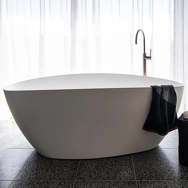 ADP Tranquil matte white freestanding bath, oval stone bath in bathroom setting with floor-mounted tap and towel