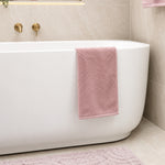 Bao Elegant white back to wall bath in a tiled bathroom, with gold wall tapware and pink towels