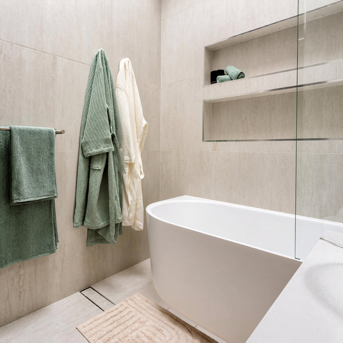 Bao Elegant white back-to-corner bath in a tiled bathroom, shown from the front-right corner with glass screen and towels