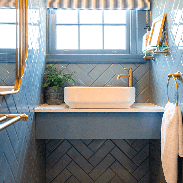 Phoenix Cromford brushed gold glass bathroom shelf mounted above a vanity basin in a blue tiled bathroom