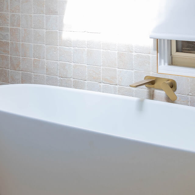 Caroma Contura II wall basin/bath mixer in brushed brass, shown mounted above a white bath against tiled wall.