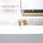 Caroma Contura II wall basin/bath mixer in brushed brass, mounted above a white bath against tiled wall