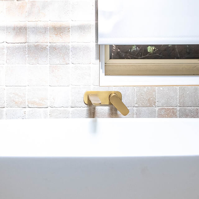 Caroma Contura II wall basin/bath mixer in brushed brass, mounted above a white bath against tiled wall