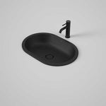 Caroma Liano II matte black pill-shaped under counter basin with matching waste, shown with tap on a grey background