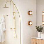 Caroma Liano II brushed brass shower mixer in a bathroom with shower rail, mirror and wall lights