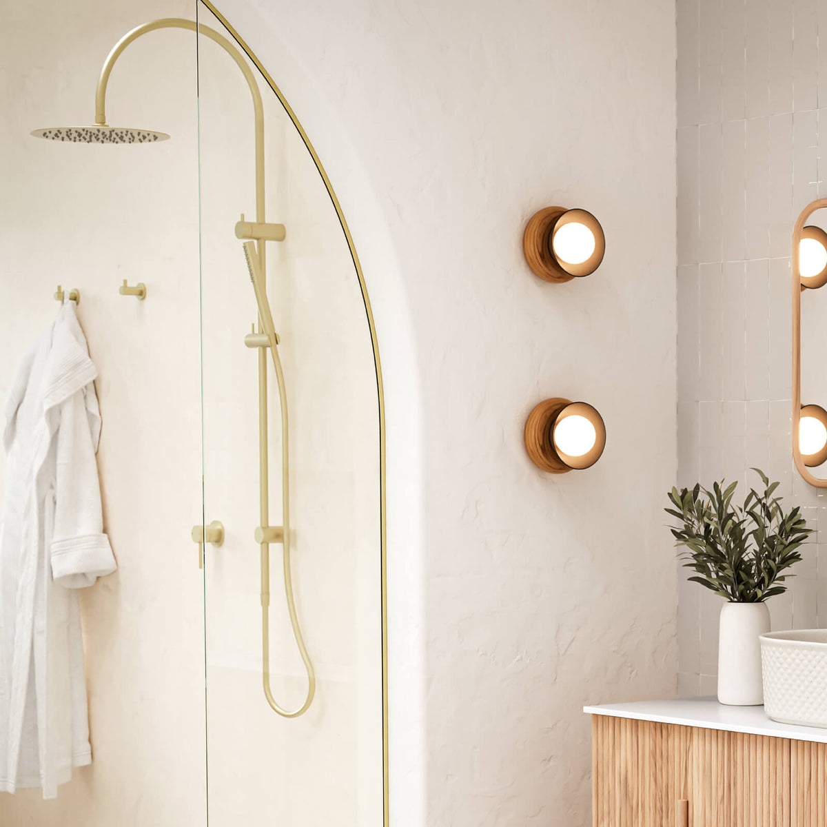 Caroma Liano II brushed brass shower mixer in a bathroom with shower rail, mirror and wall lights
