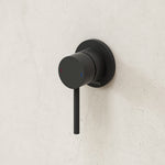Caroma Liano II matte black wall-mounted bath/shower mixer with round plate and slim lever on a light stone wall