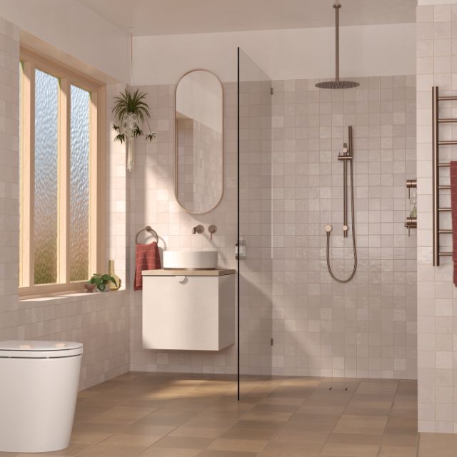 Caroma Liano II round wall mixer in brushed bronze, shown in a bathroom shower setting with matching hand shower and rose