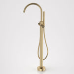 Caroma Liano II freestanding bath filler tap with hand shower in brushed brass, floor mounted with gooseneck spout and round base