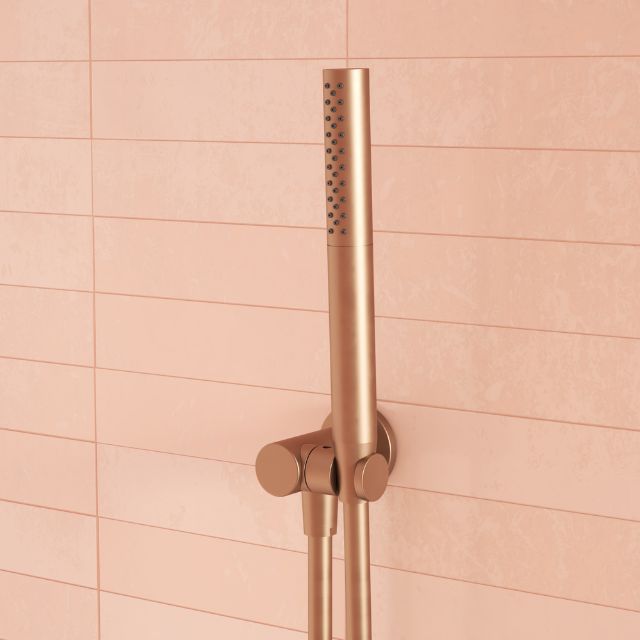 Caroma Liano II hand shower in brushed bronze, wall mounted with matching hose against pink tiled bathroom wall