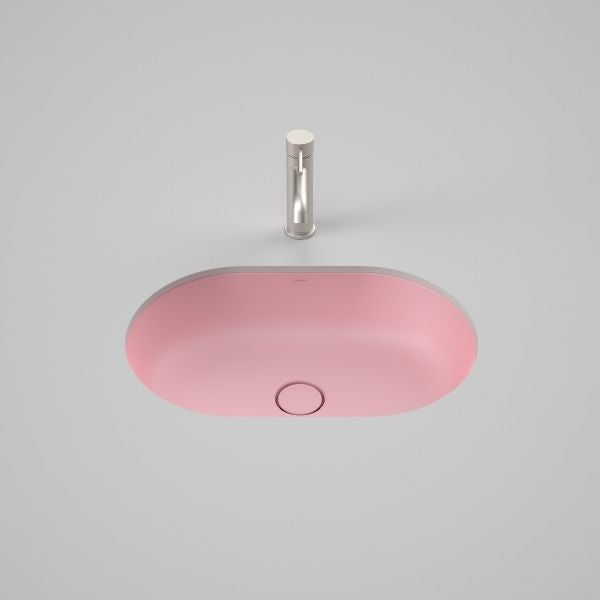 Caroma Liano II matte pink pill basin with matching ceramic pop-up waste, shown from above on a grey background