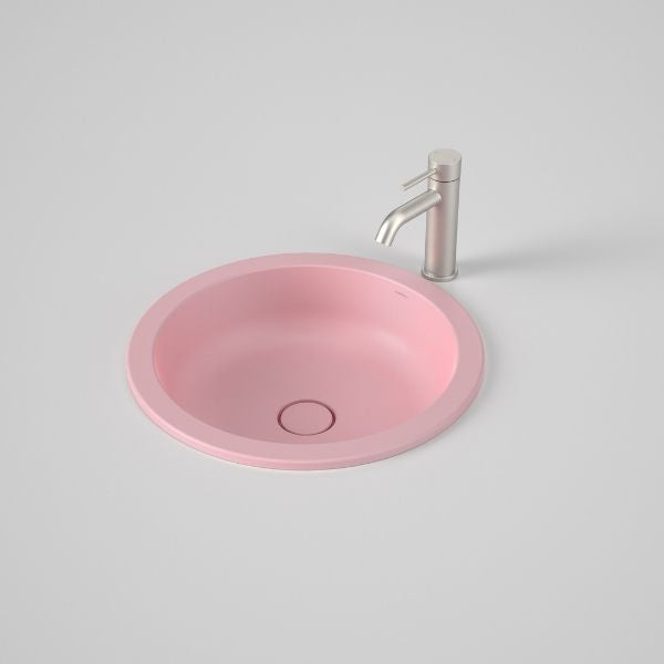 Caroma Liano II round under/over counter basin in matte pink with matching waste, shown with tap on a benchtop.