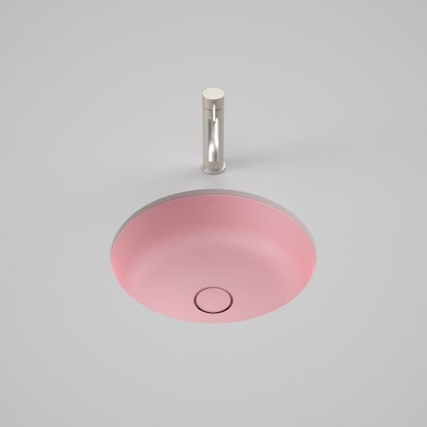 Caroma Liano II round matte pink under counter basin with matching pop-up waste, front view on grey background