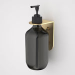 Caroma Liano II brushed brass soap bottle holder with a black bottle, wall mounted on a white background
