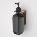 Caroma Liano II wall-mounted soap bottle holder in brushed bronze, holding a black pump bottle, side view